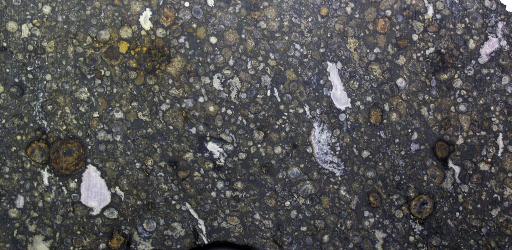Coupe de la chondrite carbonée Allende montrant chondres et inclusions blanches CAI