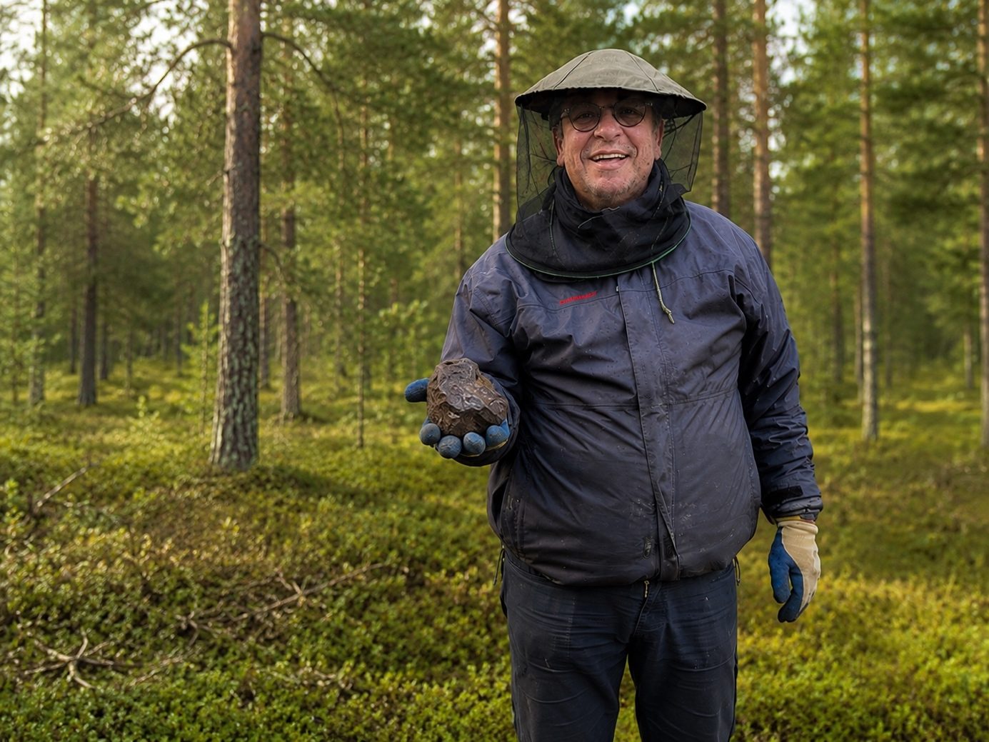 Un homme au milieu d'une forêt en Laponie tenant une météorite Muonionalusta