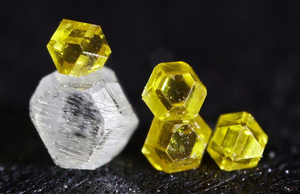 Cristaux bruts de diamant synthétique, un incolore et quatre jaunes, sur fond noir