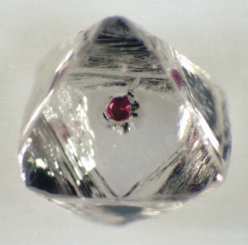 Octaèdre de diamant brut transparent contenant une petite inclusion de grenat rouge vif en son centre.