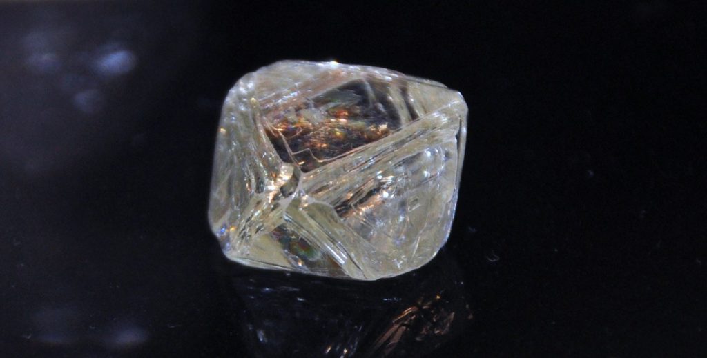 Cristal de diamant brut octaédrique transparent posé sur fond noir