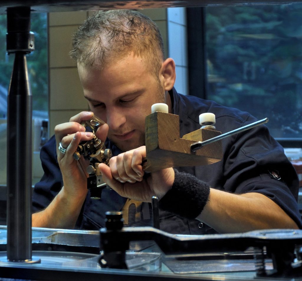 Tailleur de diamants examinant une pierre montée sur un dop, tang en main, au-dessus du scaife