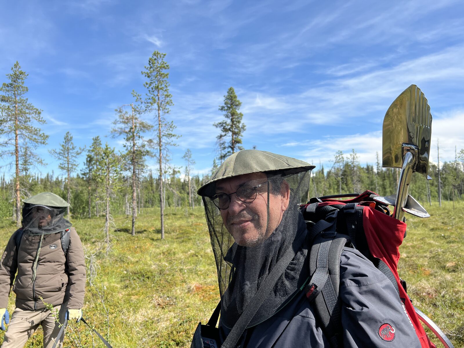 Ramon Cortes en Laponie avec moustiquaire de tête, sac à dos et pelle, forêt boréale en arrière-plan